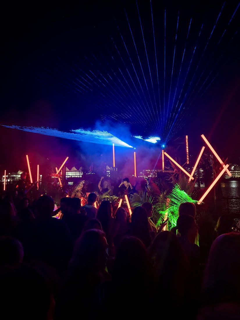 Laser fan and red LED tubes above a dancing crowd outdoors